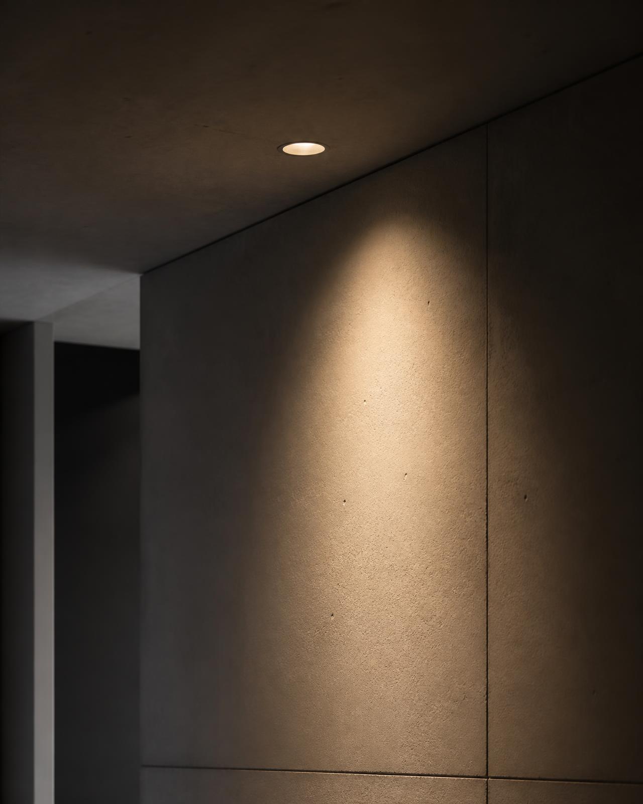 Recessed architectural downlight washing a concrete wall with warm light